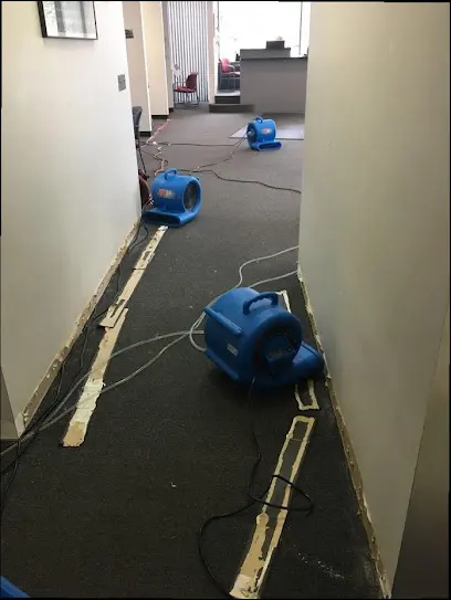 Air movers lined along a hallway with baseboards removed during a Mission Viejo dry-out
