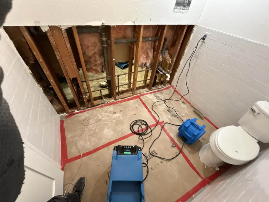 Bathroom wall opened to the framing with a dehumidifier and air mover running